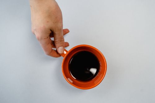 Free A hand holding an orange coffee mug viewed from above on a white background. Stock Photo