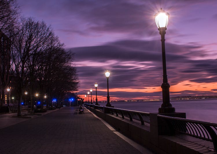 Photography Of Turned On Street Lamps Beside Bay During Night Time