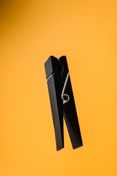 Minimalist photo of a black clothespin against a bold yellow backdrop.