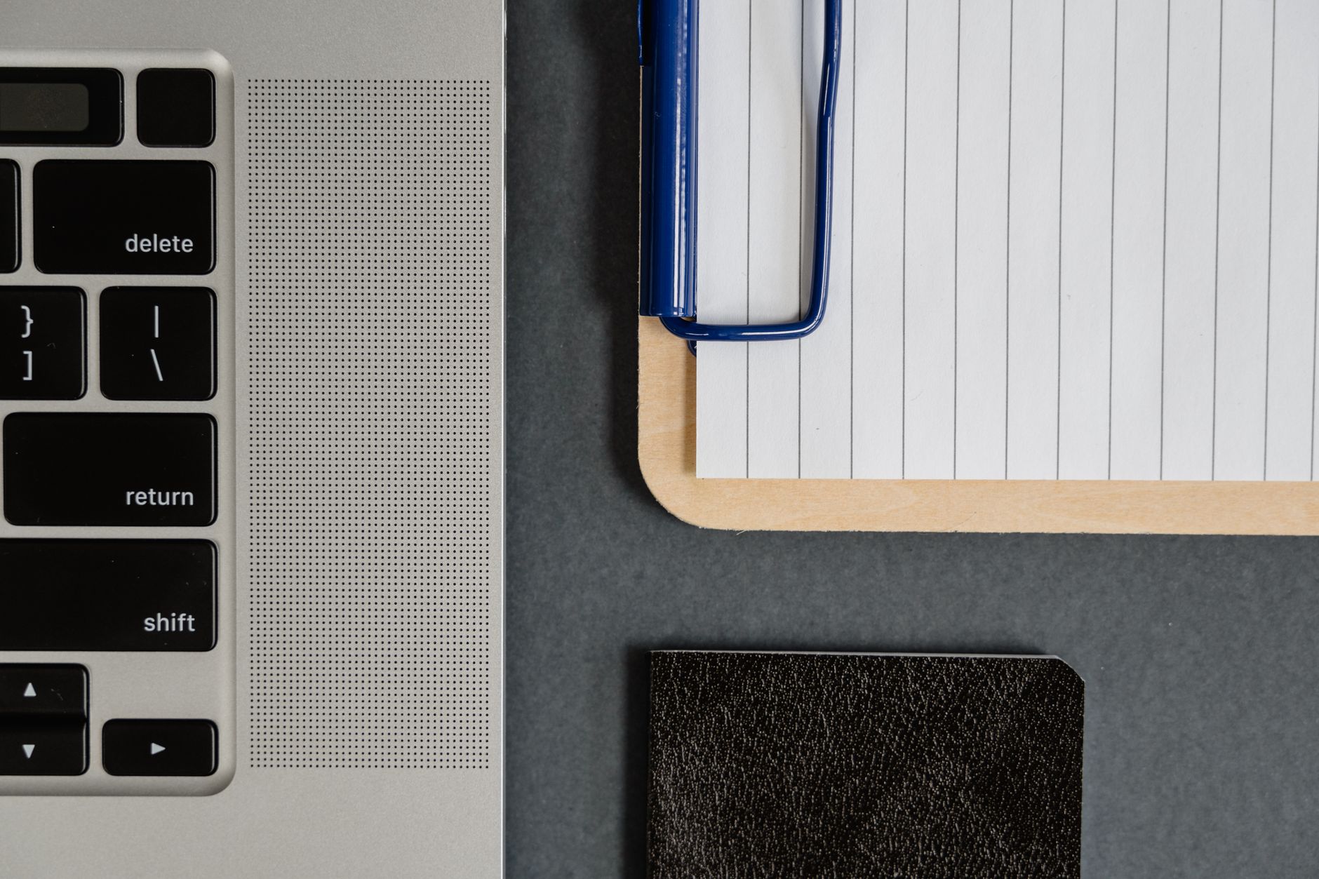 Flat lay of a laptop, lined paper on clipboard, and notebook on a desk.