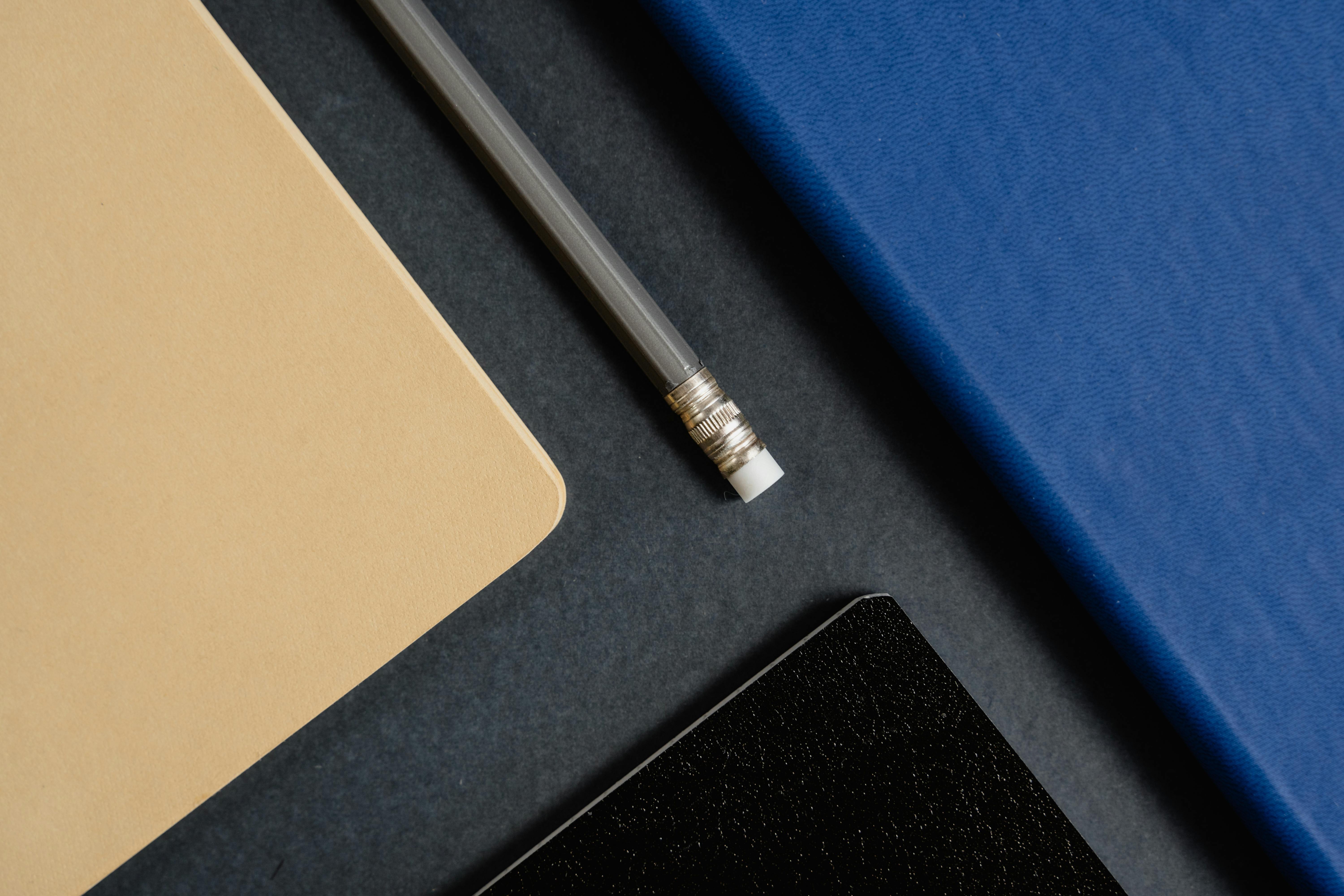 Close-up still life image featuring a pencil and colorful notebooks on a dark background.