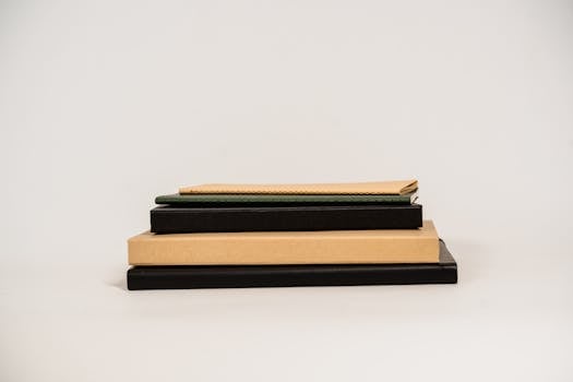 Close-up of a stack of books and notebooks on a plain white background, showcasing various covers and bindings.
