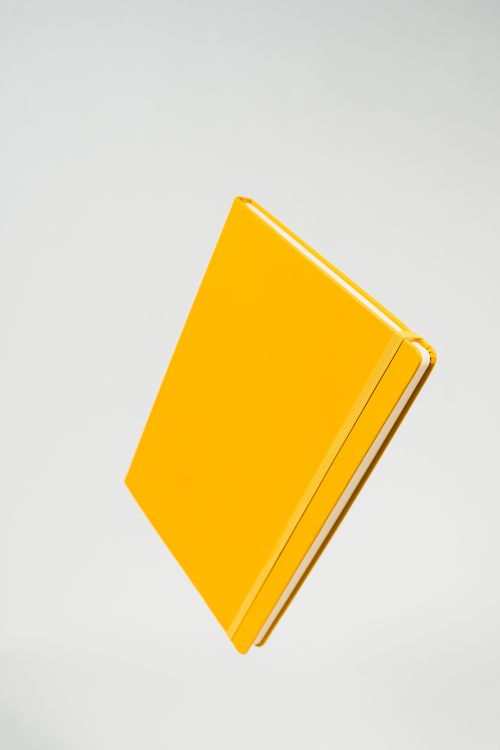 Free Minimalist shot of a bright yellow notebook suspended against a neutral background. Stock Photo