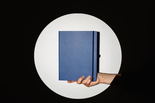 A hand holding a blue notebook against a black backdrop with a spotlight highlighting the subject.