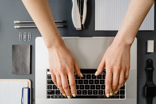 Hands typing on a laptop surrounded by office stationery. Minimalist workspace.