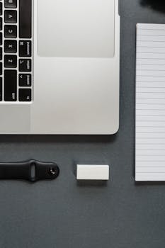 Top view of a workspace featuring a laptop, notebook, and accessories on a gray surface.