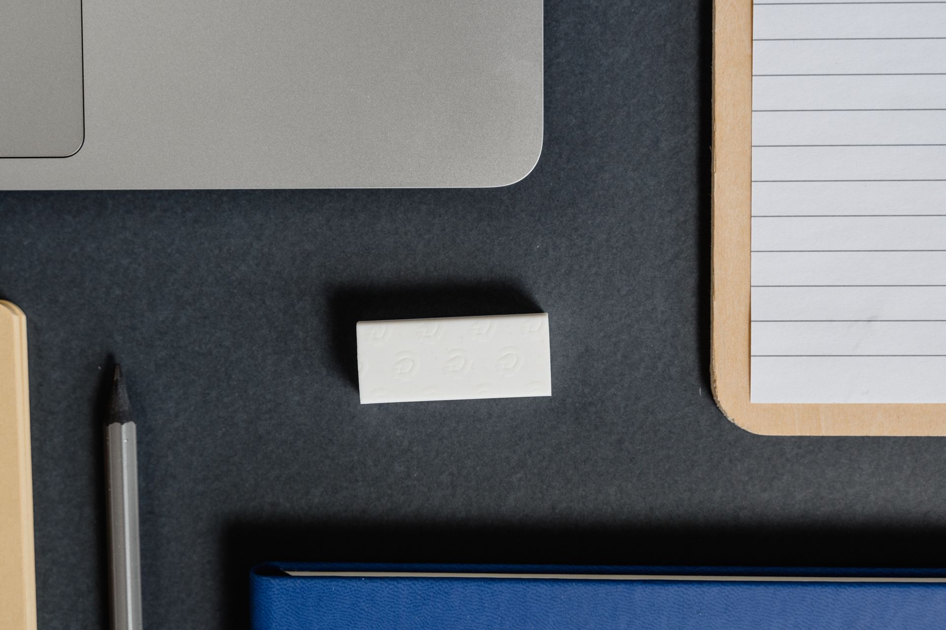 Top view of a laptop, notepad, pencil, and rubber eraser on a dark surface, perfect for office themes.