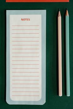 Minimalist notepad and pencils arrangement on a green background, perfect for stationery lovers.