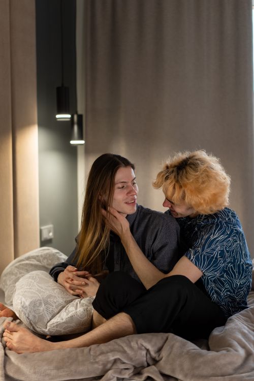 Free A loving couple sits closely on a bed, sharing an affectionate moment in a cozy bedroom. Stock Photo