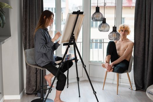 A couple enjoying artistic activities at home, one painting the other sitting.