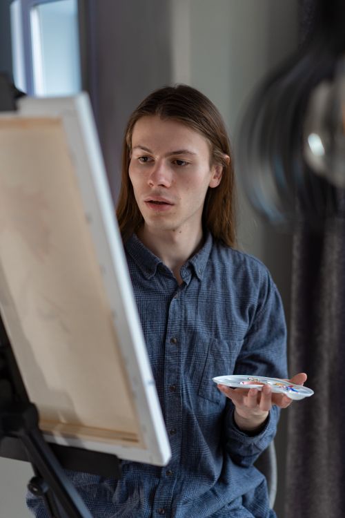 Free Caucasian male artist in blue shirt focusing on painting in a studio. Stock Photo