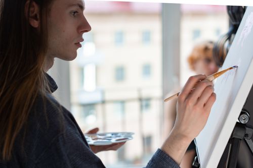 Free Portrait of a concentrated artist with long hair painting on a canvas indoors. Stock Photo