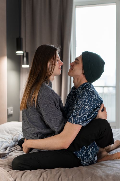Free A young couple embraces on a bed, bathed in soft natural light, capturing a moment of intimacy and connection. Stock Photo