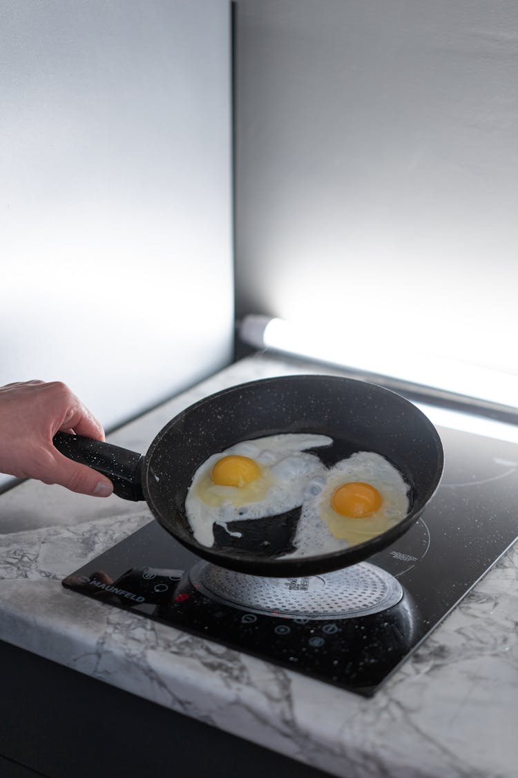 A Person Holding A Pan With Cooked Eggs