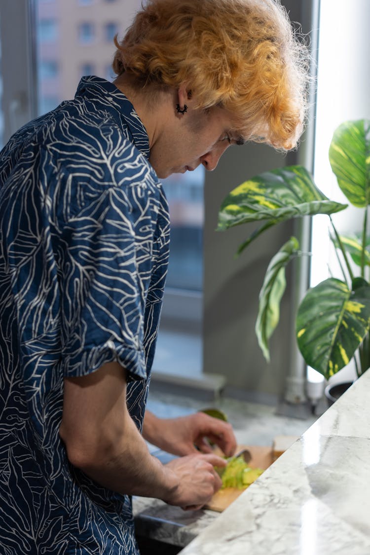 Man In A Printed Blue Shirt Slicing Food 