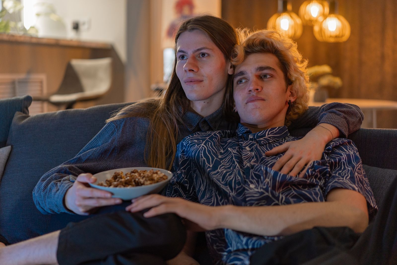 Two people sitting together on a sofa with a bowl of popcorn