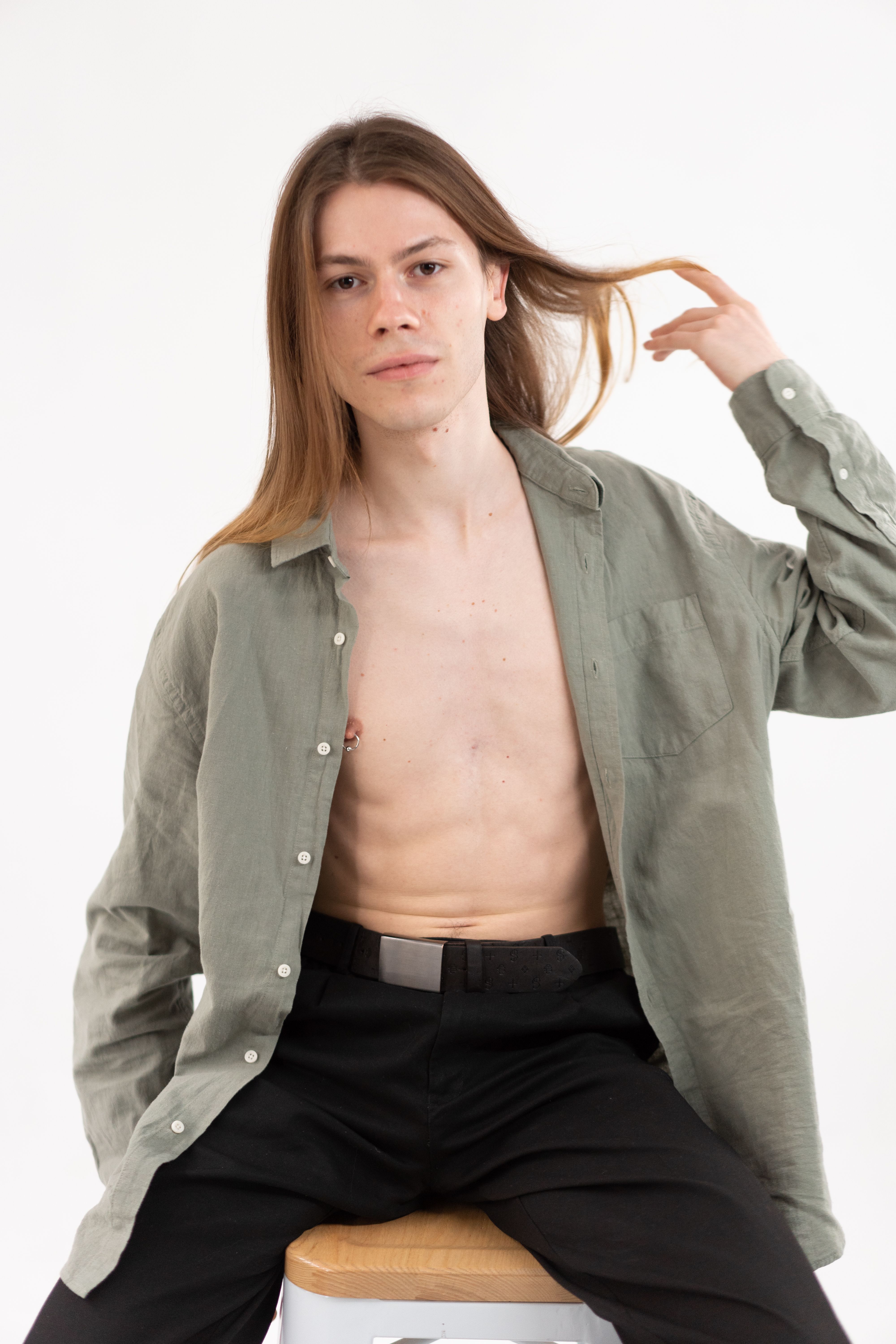 Portrait of a young adult with long hair wearing an open green shirt, studio setting.