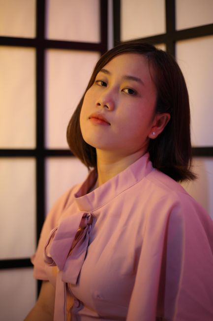 Young ethnic female in elegant pink blouse with dark hair looking at camera on blurred background