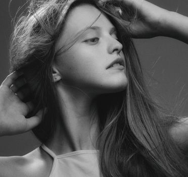 Artistic black and white portrait of a woman with hands in hair, showcasing elegance.
