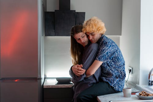Free Man Sitting on Kitchen Counter Hugging Another Man Stock Photo