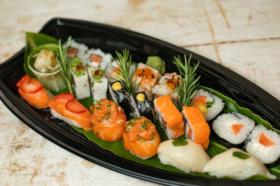 Black sushi boat on banana leaf with salmon nigiri, salmon rolls, maki, pickled ginger and rosemary