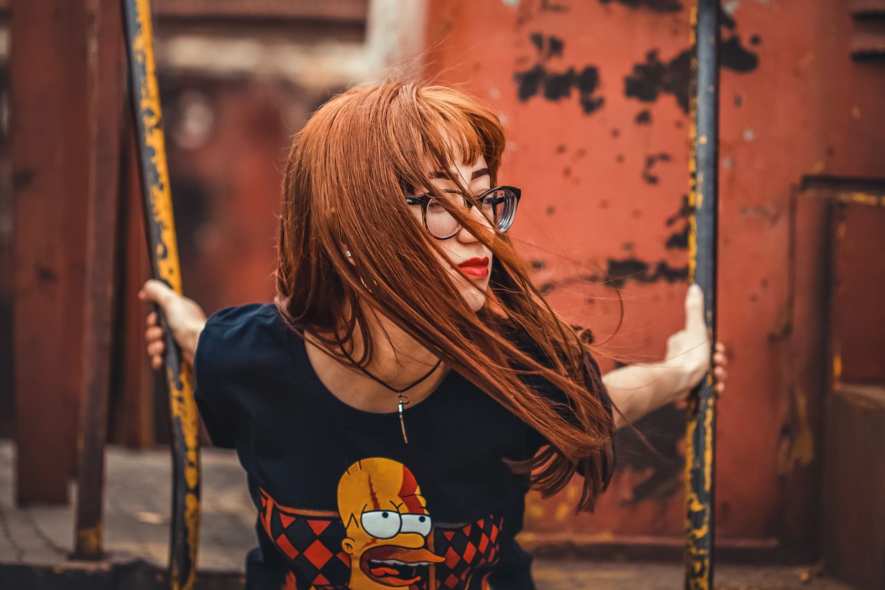 woman with red hair in glasses wearing a graphic t shirt poses near a