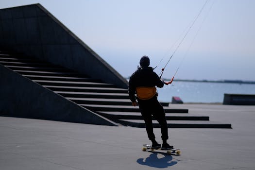 Man kiteboarding on a skateboard near water in Denmark, showcasing urban adventure.