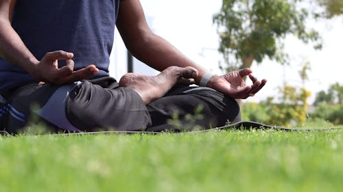 A Person Meditating on Green Grass Field