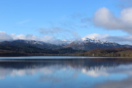 清澈的蓝天和轻云下，宁静的湖面倒映着白雪皑皑的山脉