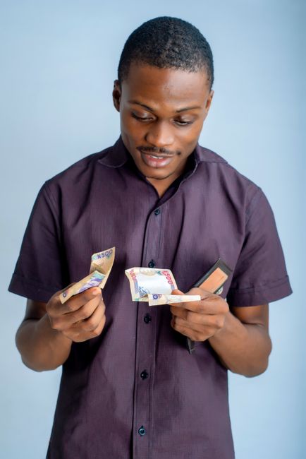 African man in a studio counting Nigerian naira banknotes with a wallet in hand. African man in a studio counting Nigerian naira banknotes with a wallet in hand.
