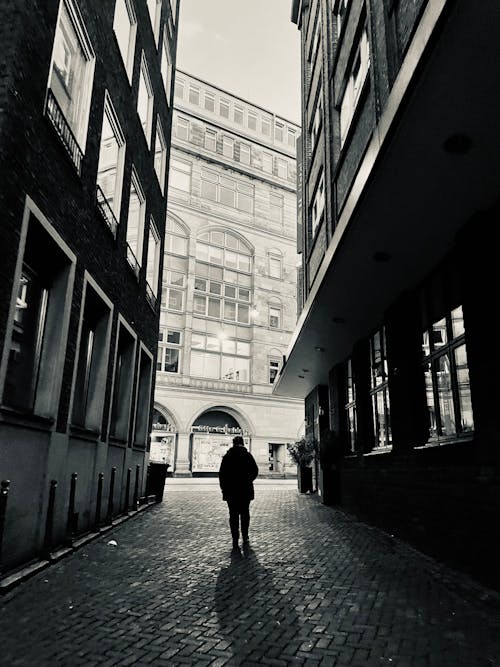 Monochrome Photo of a Person Walking on an Alley