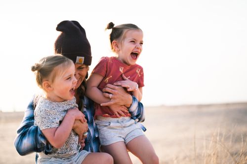Free A happy mother embraces her giggling daughters outdoors on a sunny day, capturing pure joy and togetherness. Stock Photo