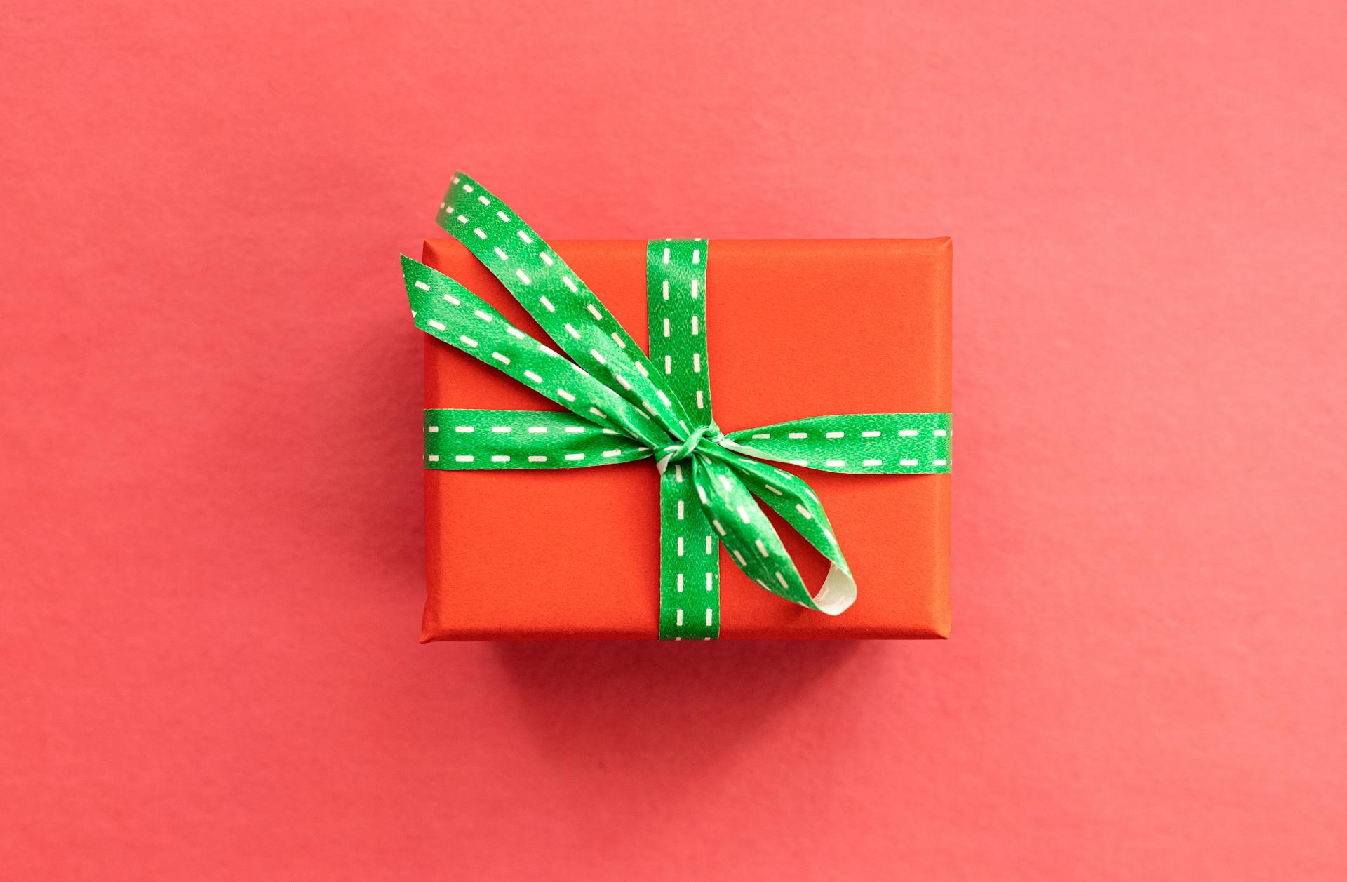 A vividly wrapped gift box with a green ribbon placed on a red background, ideal for holiday themes.