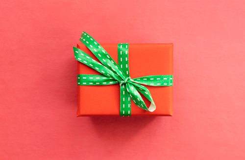 Free A vividly wrapped gift box with a green ribbon placed on a red background, ideal for holiday themes. Stock Photo
