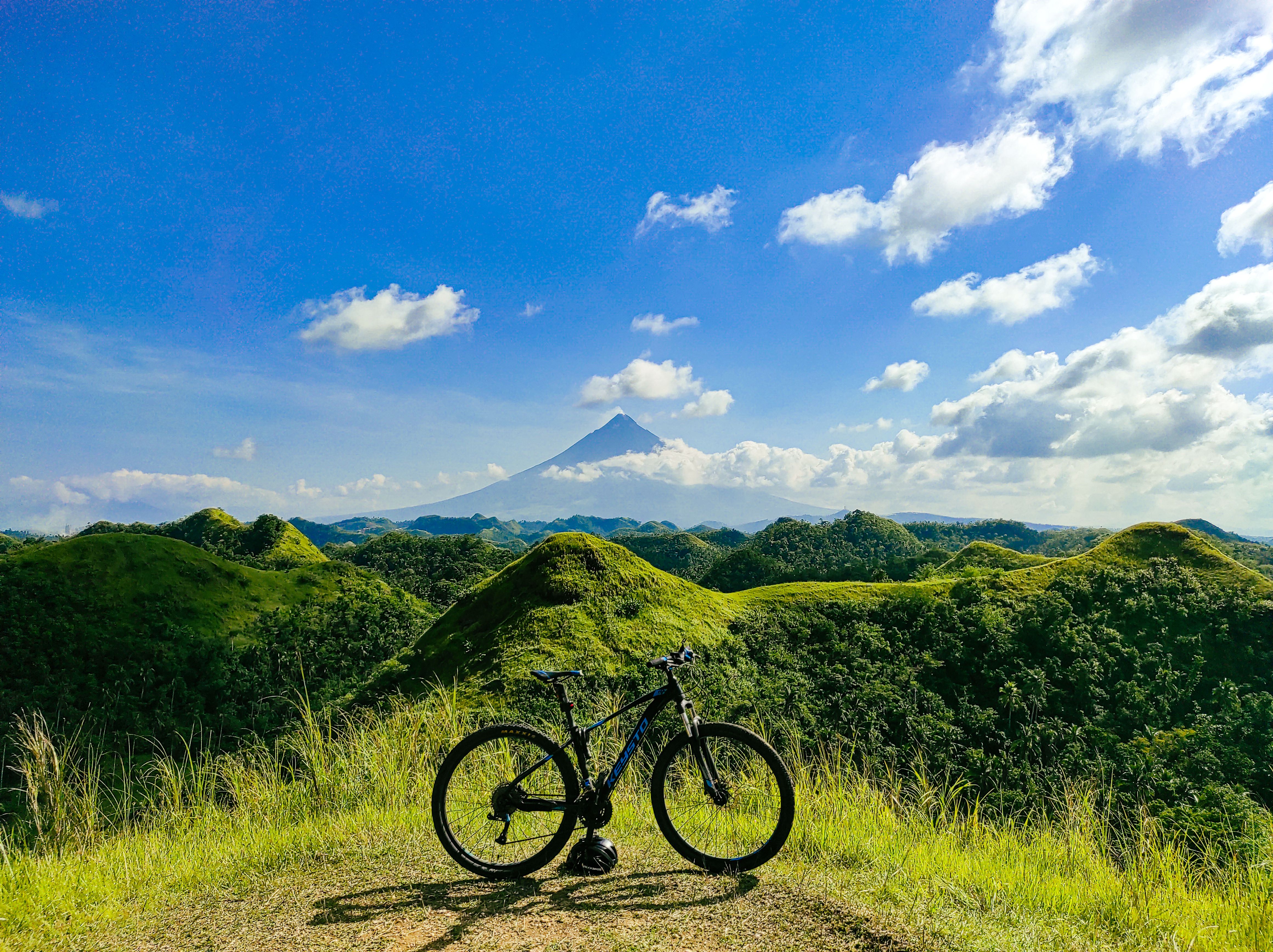 Bicycle parked on grassy hill with scenic view of mountains and clear blue sky.