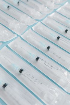 High-angle shot of sterile syringes in individual packaging arranged on a blue surface.