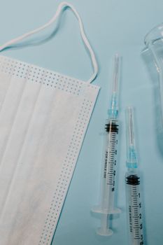 Close-up of face mask and syringes on a blue surface, illustrating healthcare themes.