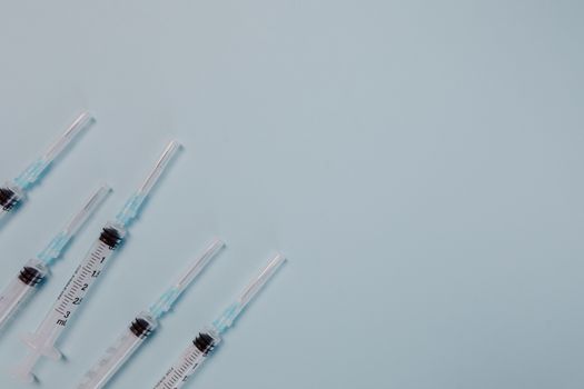 Close-up of multiple syringes on a blue background, featuring ample copy space.