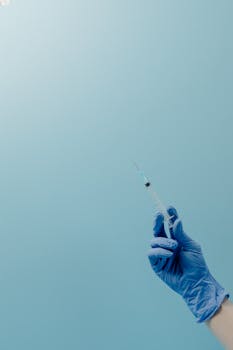 Close-up of a blue gloved hand holding a syringe against a blue background, symbolizing healthcare.