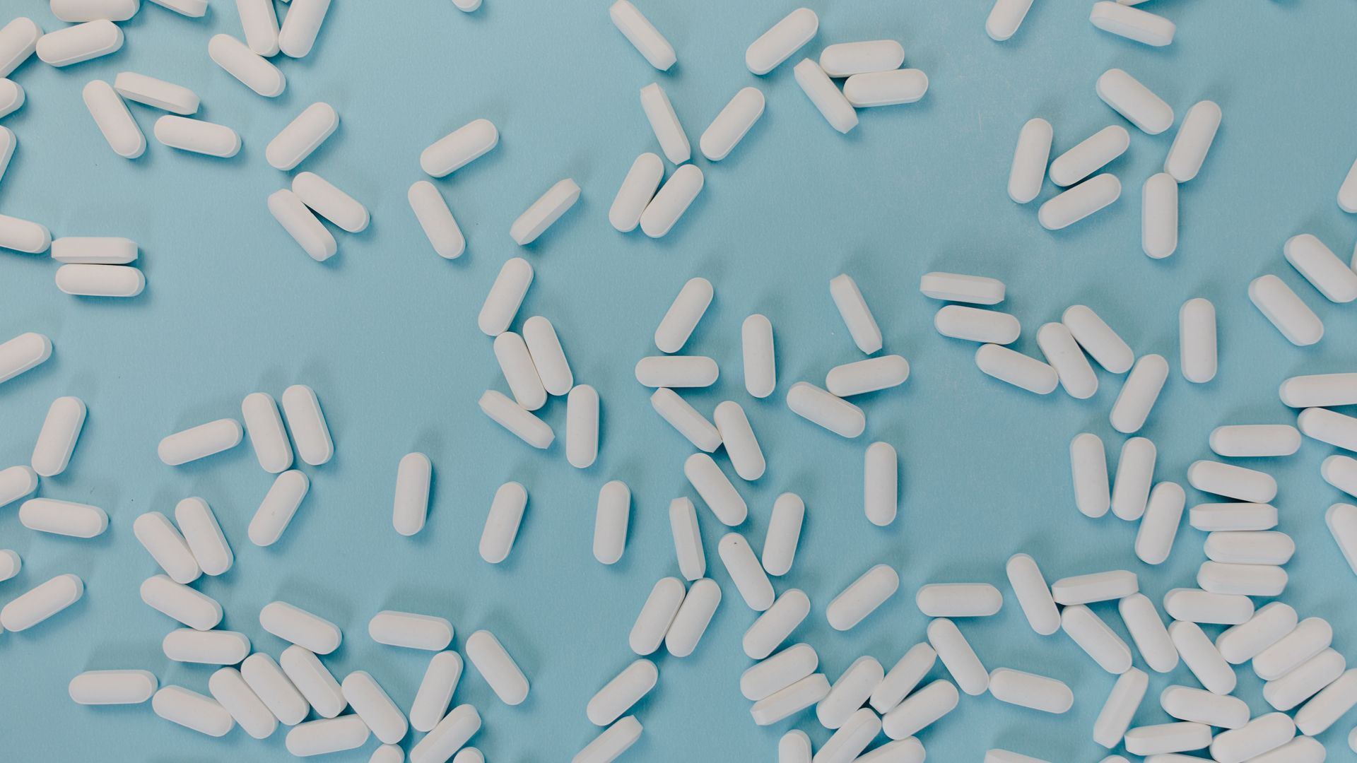 Modafinil vs Strattera: Unlocking Cognitive Potential Top view of scattered white pills on a blue surface, representing healthcare and medicine — modafinil vs strattera