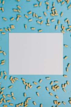 Top view of scattered pills around a blank paper on a blue backdrop.