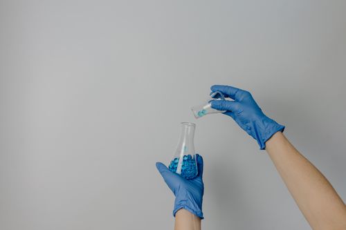 Free Close-up of hands with gloves pouring blue chemicals in a lab setting. Stock Photo