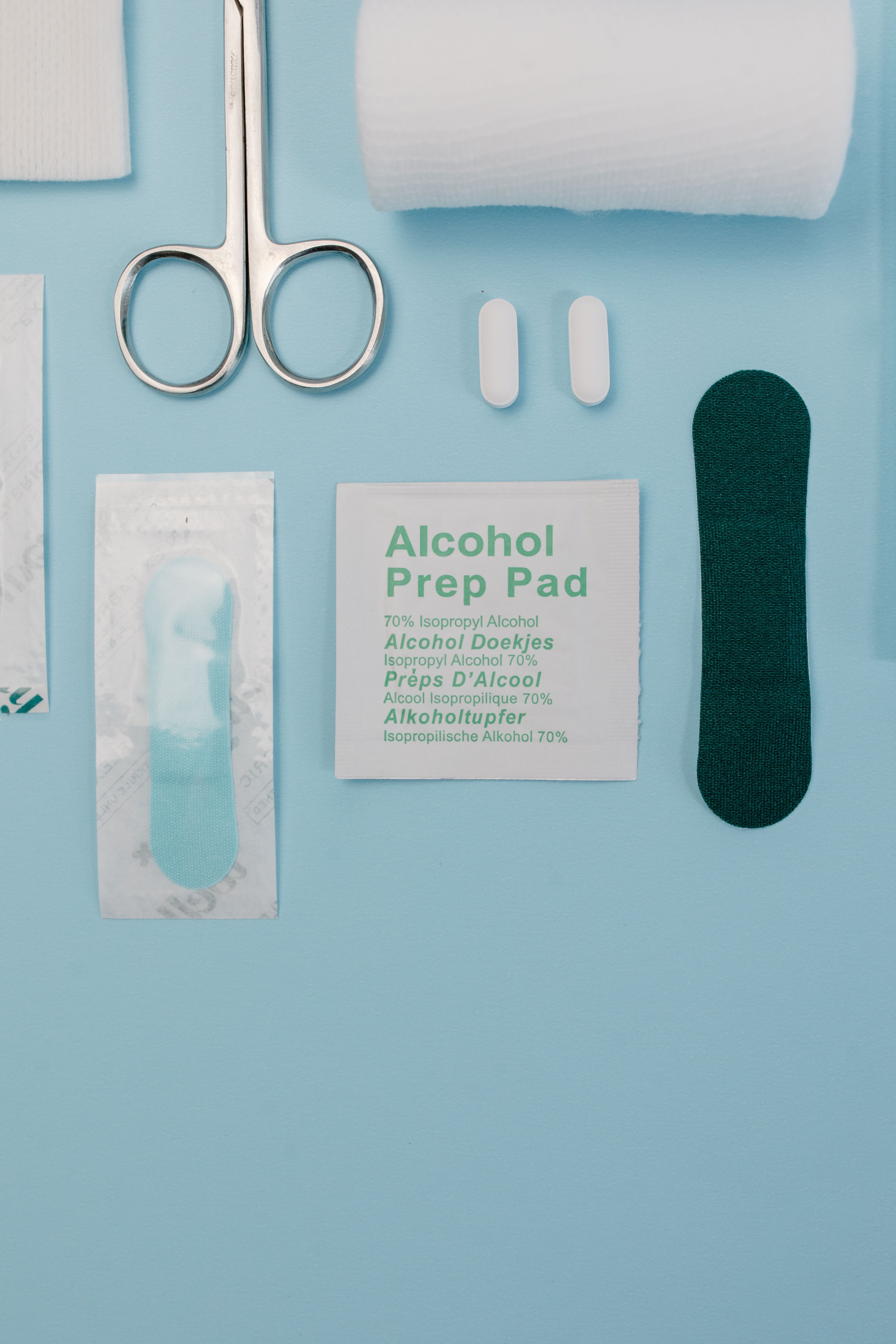 Top view of medical supplies including gauze, scissors, and alcohol prep pad on blue background.