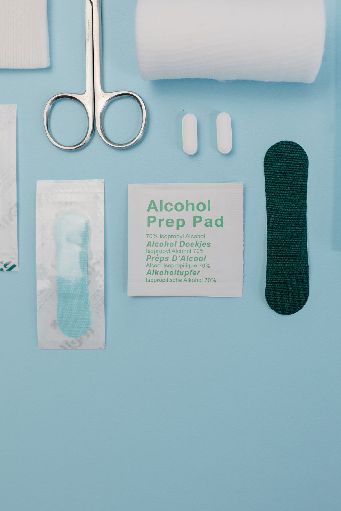 Gauze pads, scissors, and alcohol prep pads laid out on a blue surface