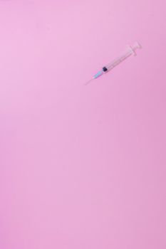 Close-up of a syringe on a pastel pink background, offering ample copy space.