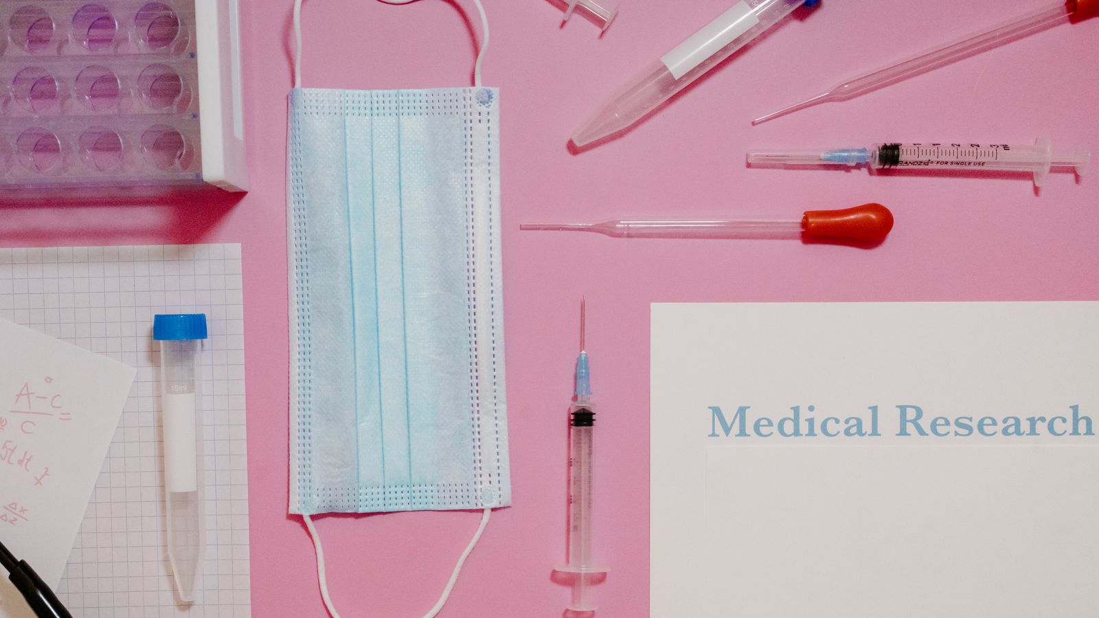Flat lay of medical research tools and supplies on a pink background.