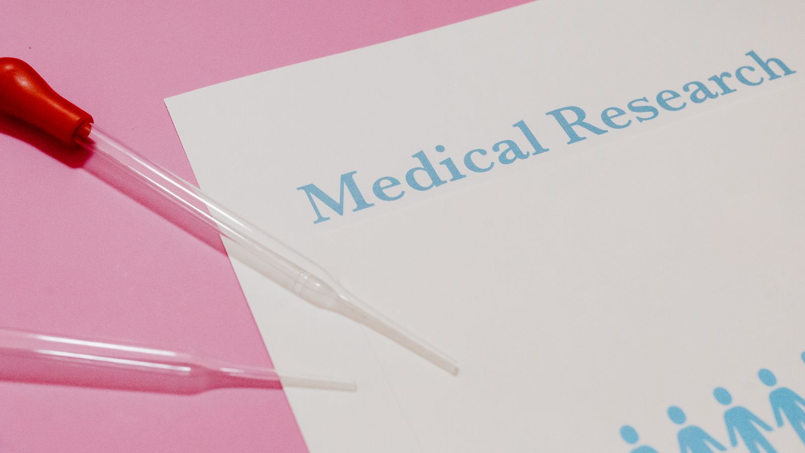 Close-up of a medical research document and pipette on a pink surface, highlighting scientific research and healthcare.