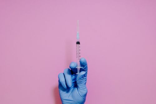 Free A blue-gloved hand holding a syringe against a pink background, symbolizing medical care. Stock Photo