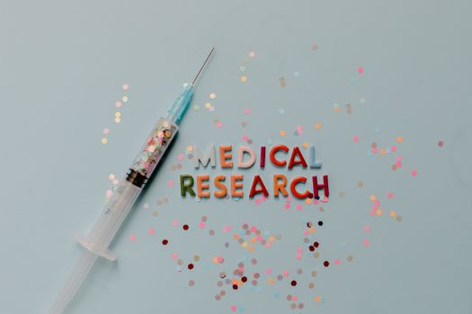 Close-up of a syringe with colorful confetti on medical research theme.
