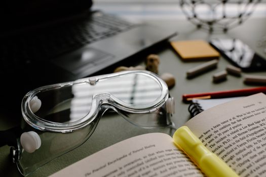 Close-up of lab goggles with an open book and study materials in a science lab setting.